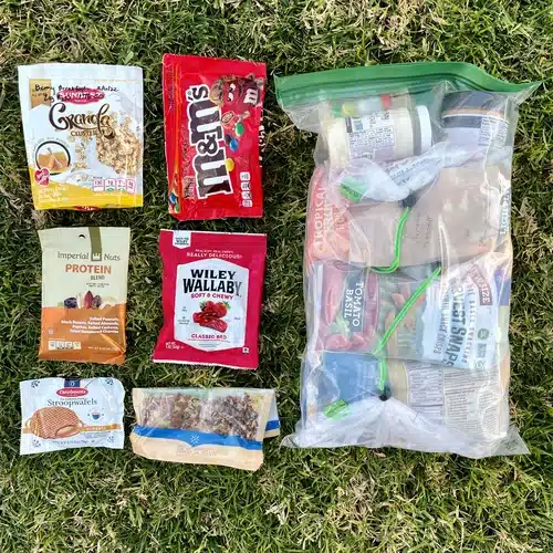 Four-day backpacking food supply with three days stored in an odor-proof bag and one day’s meals laid out separately. Reused snack bags shown as eco-friendly packaging alternatives.