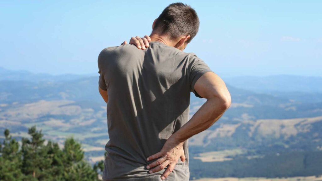 Hiker rubbing his neck and back due to exercise-induced inflammation.