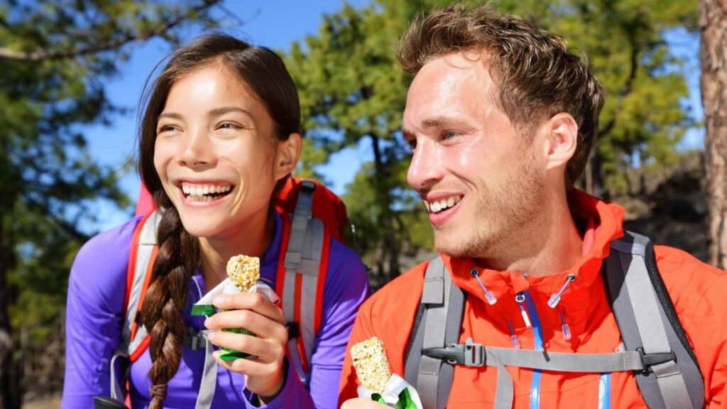 Two hikers holding granola bars after learning how to choose snacks for hiking.