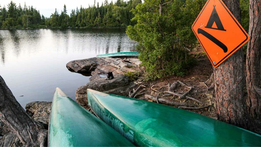 Canoes lined up at the edge of the water next to a canoe camping sign