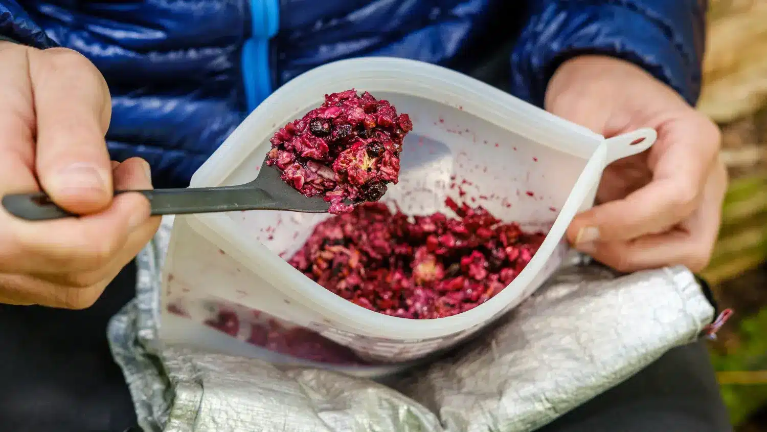 Backpacker eating rehydrated berry breakfast crumble from a reusable pouch in the backcountry