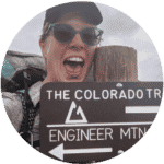 Excited backpacker smiling next to a Colorado Trail sign at Engineer Mountain, wearing sunglasses and a hiking pack.