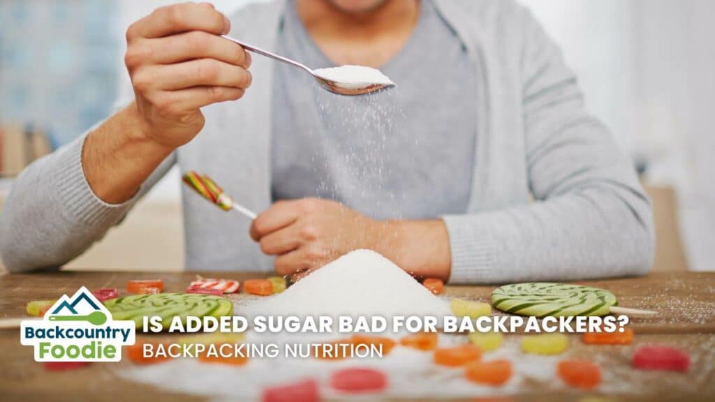 Is Added Sugar Bad For Backpackers Backcountry Foodie Blog person holding teaspoon of sugar with candy on the table