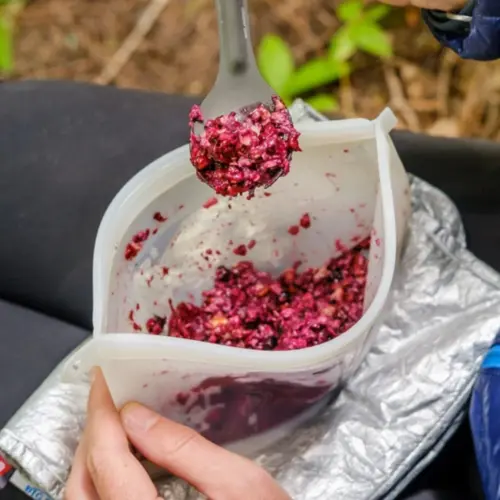 Prepared Berry Breakfast Crumble backpacking recipe served in a silicone bag on the hiker's lap with ferns nearby