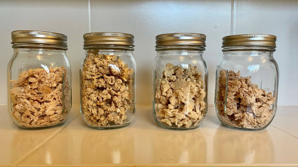 Four glass mason jars filled with dehydrated canned tuna for long-term storage to be used for DIY backpacking meals.