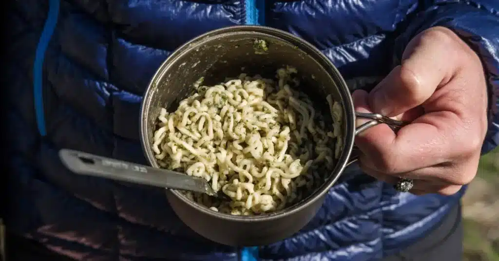 Backpacker holding a metal mug filled with ultralight pesto ramen – easy trail meal idea.