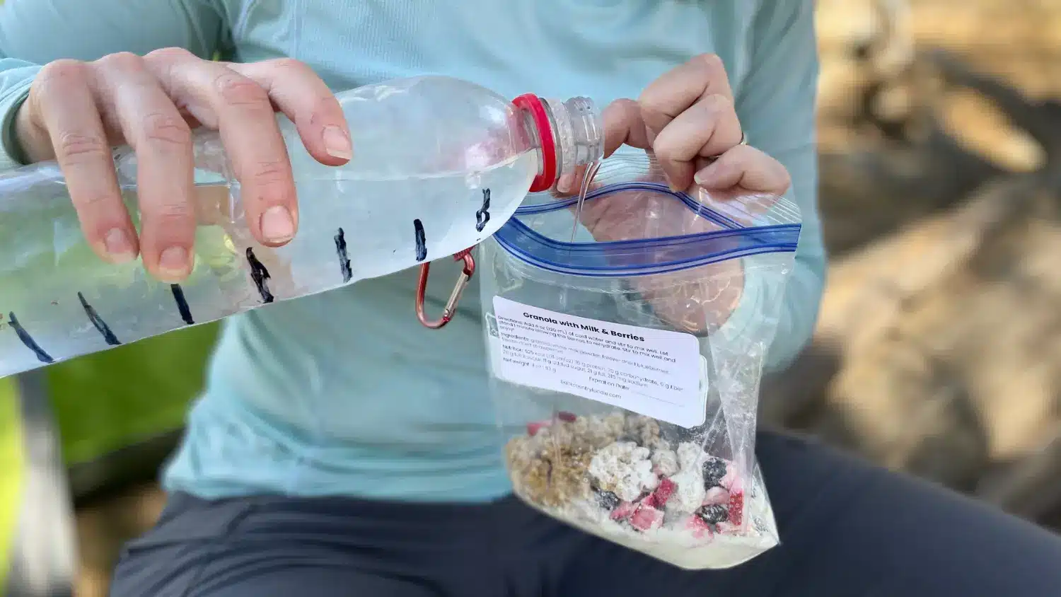 Backpacker pouring water from a plastic bottle into a zip-top bag filled with granola, powdered milk, and freeze-dried berries to make a no-cook backpacking breakfast.