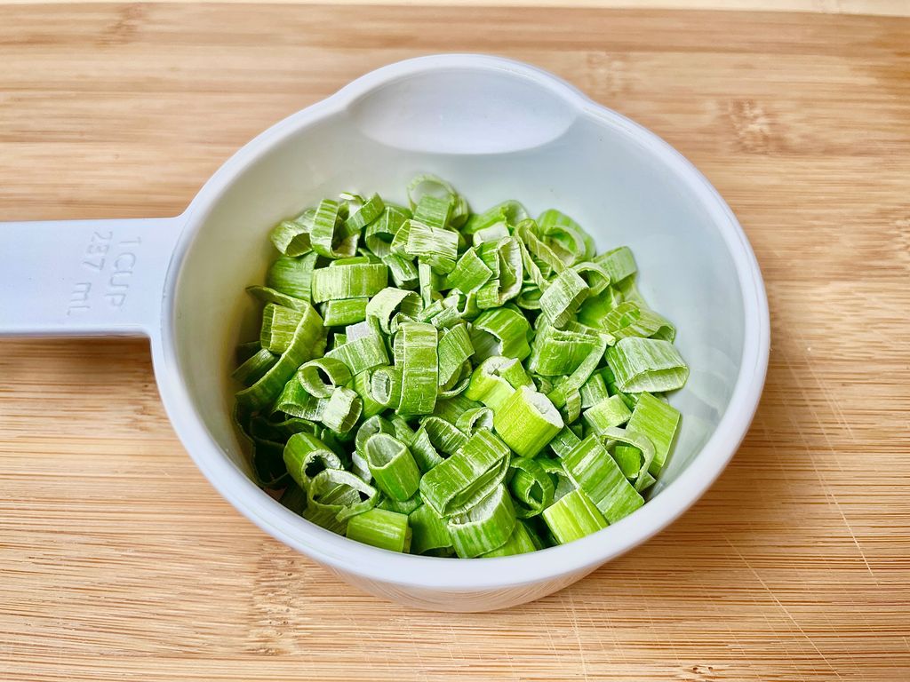 Freeze dried scallions in a white measuring cup for DIY freezer bag cooking meals