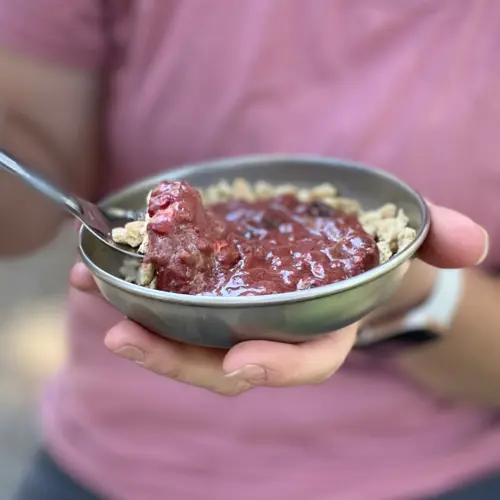 Backpacker holding a camping bowl of prepared Mixed Berry Crumble backpacking recipe with a spoonful lifted to eat