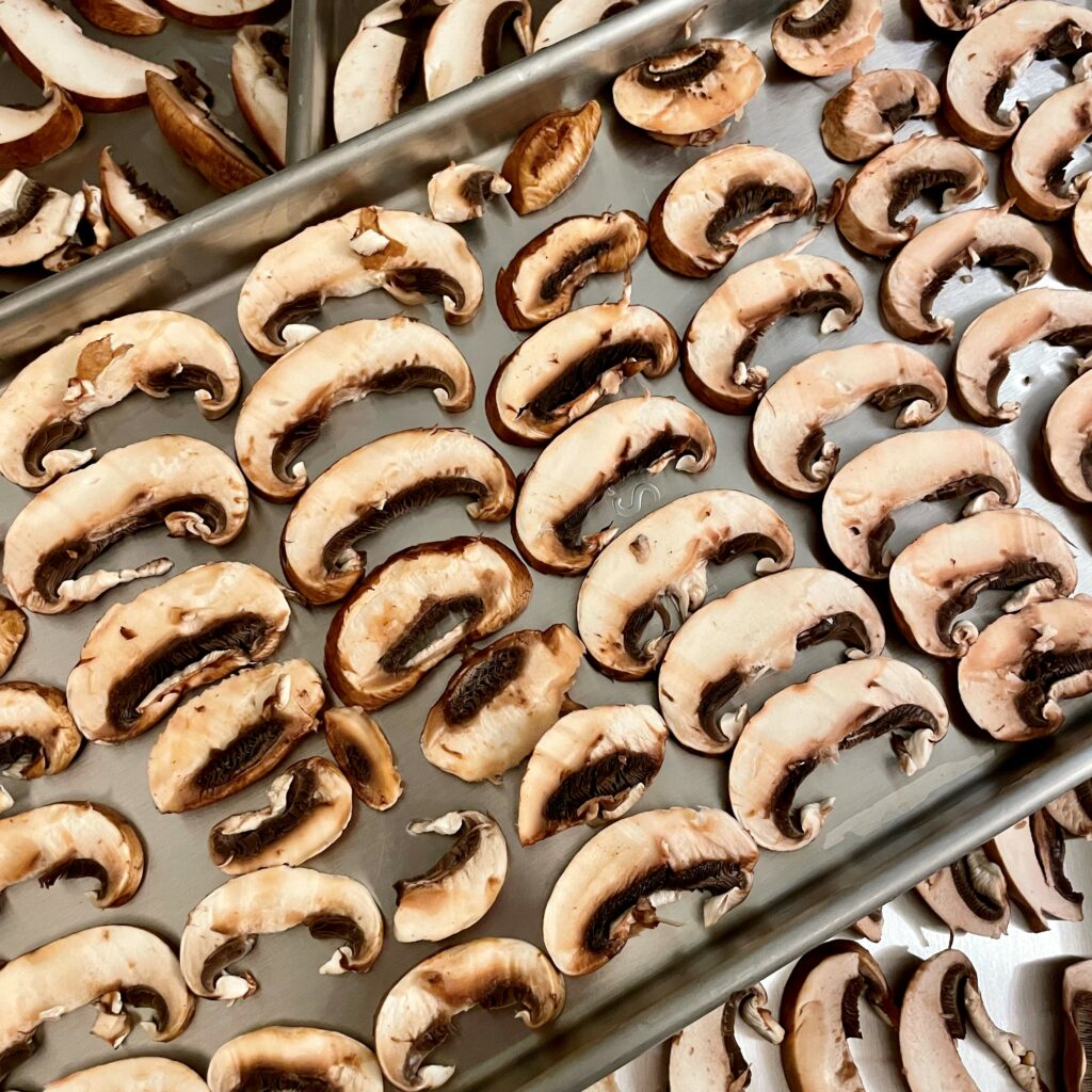 Sliced mushrooms on Harvest Right freeze dryer trays to be freeze dried for backpacking meals.