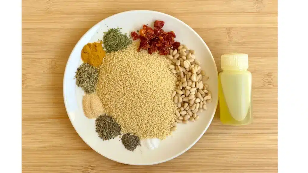 Plate with dry ingredients for a backpacking couscous recipe, including couscous, pine nuts, sun-dried tomatoes, dried herbs, spices, and a small bottle of olive oil on the side.