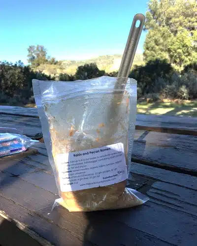 Backpacking meal bag of Raisin and Pecan Ramen sitting on a picnic table with titanium spoon, used during a Pacific Crest Trail hike when the hiker experienced bonking from underfueling.