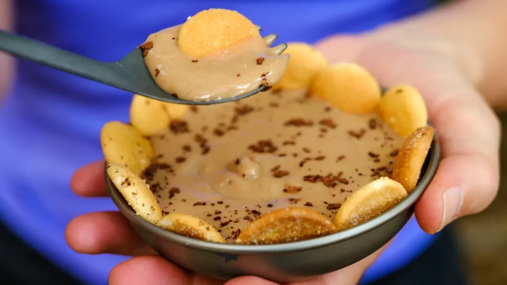 Trail-friendly tiramisu dessert in a small camping bowl, topped with crushed chocolate and lined with vanilla wafer cookies